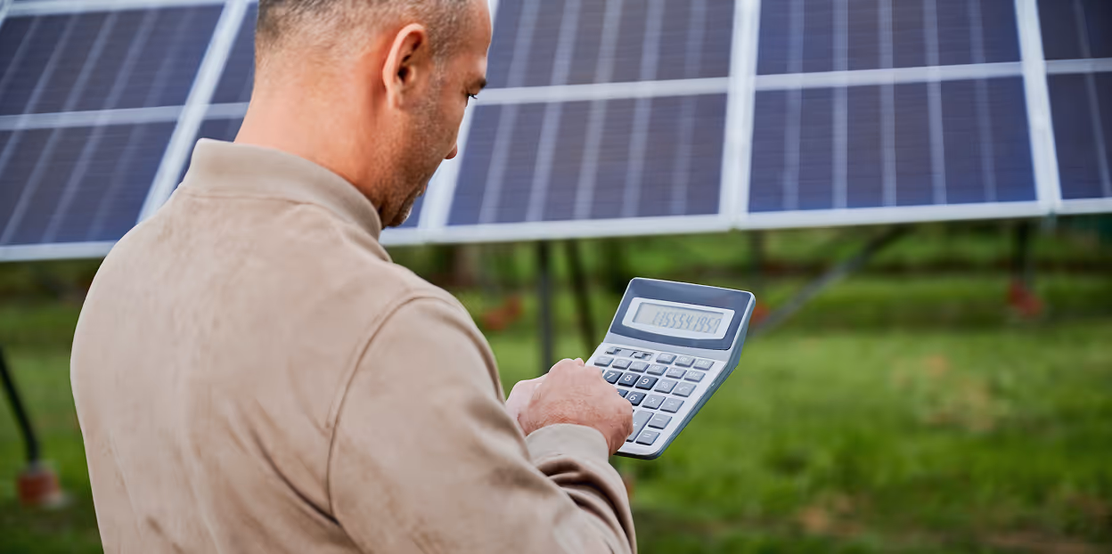 Man using a calculator outdoors with solar panels visible in the background.