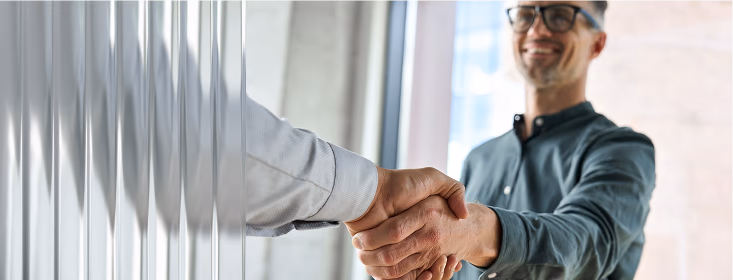 Two men shaking hands through partially frosted glass, one man smiling in background.