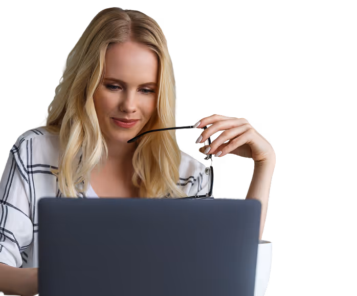 Blonde woman holding eyeglasses and looking at a laptop screen.