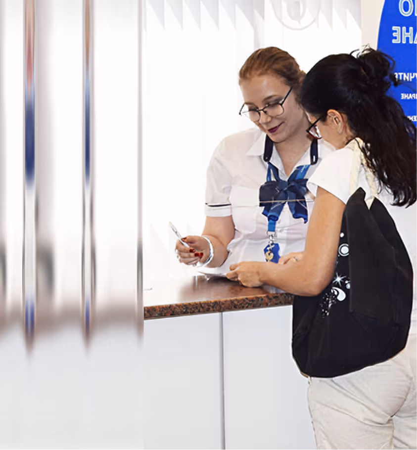 Two women talking at a counter, one in uniform with a badge and the other holding a phone and wearing a black backpack.
