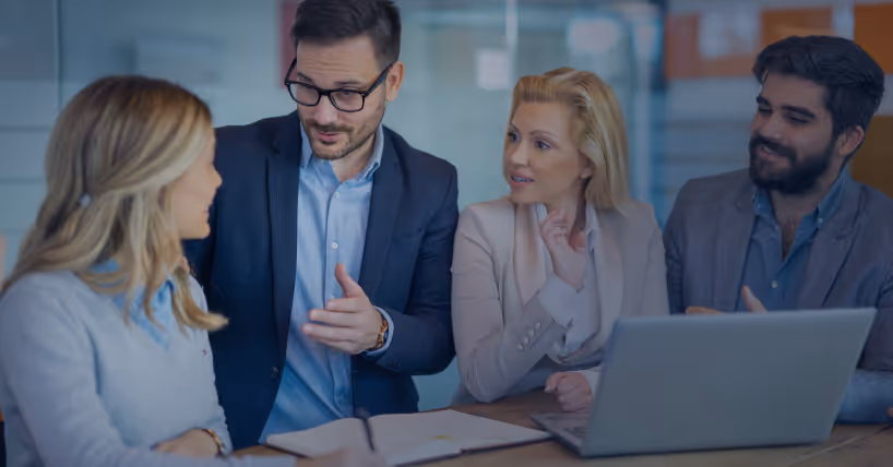 Four business professionals having a discussion around a table with a laptop and notebooks.