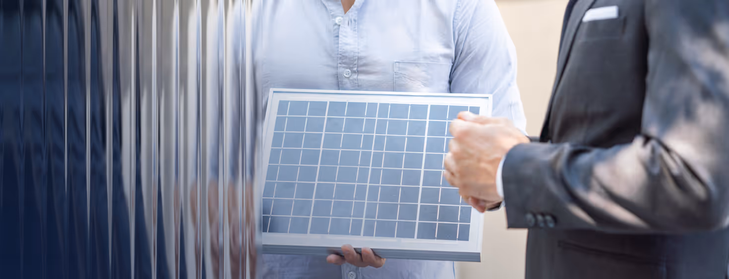 Person in white shirt holding a small solar panel while another person in a suit gestures nearby.