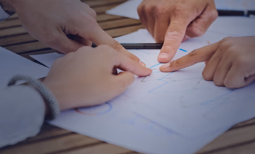 Three hands pointing at a document with charts and graphs on a wooden table during a discussion.