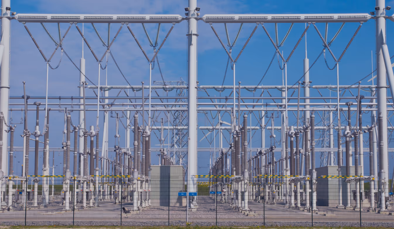 Electrical substation with transformers, insulators, and high voltage power lines under a clear blue sky.