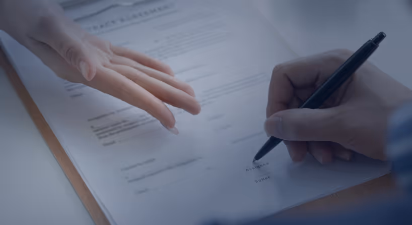 Close-up of a hand pointing and another signing a document with a pen.