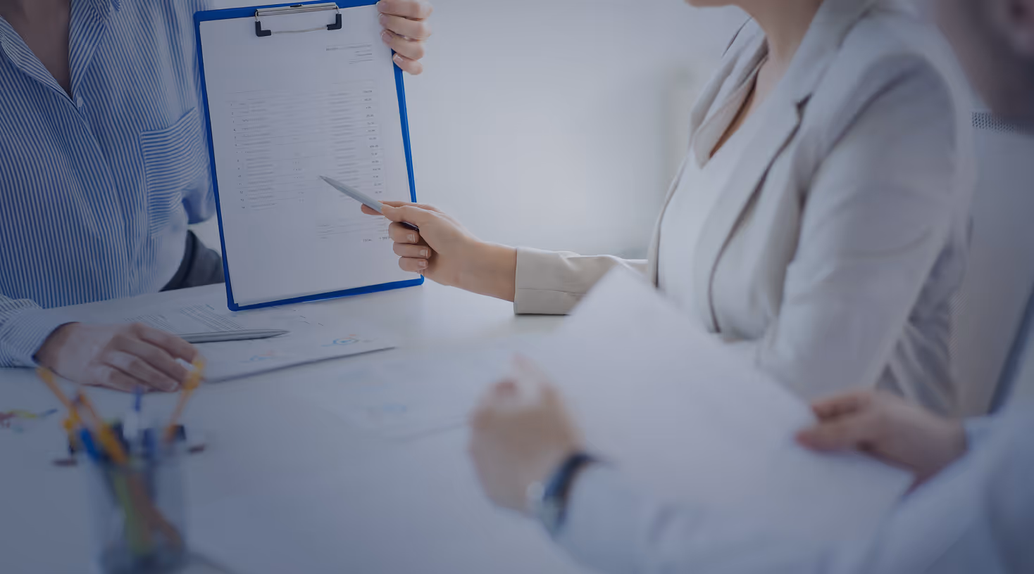 Three professionals discussing a document on a clipboard at a meeting table.