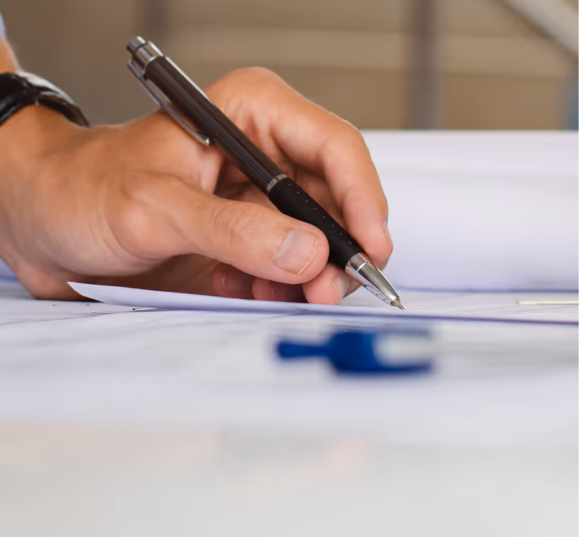 Person holding a black pen poised to write on white paper on a table.