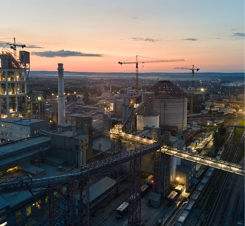 Industrial complex with cranes and large storage silos at sunset under a colorful sky.