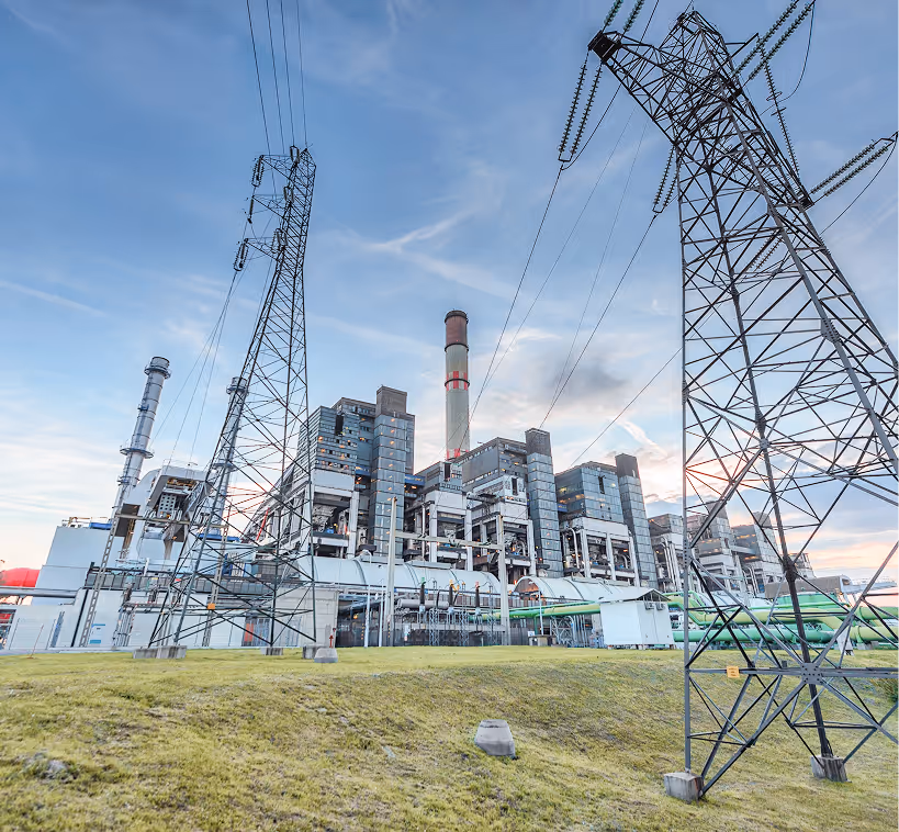 Industrial power plant with metal towers and electrical wires against a blue sky.