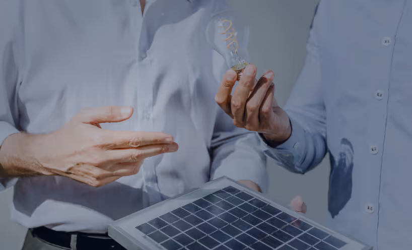 Two individuals in shirts holding a small solar panel and a glowing light bulb, symbolizing renewable energy.