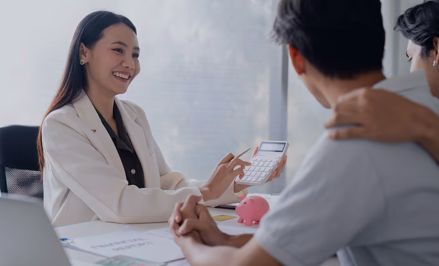Smiling female consultant using a calculator while discussing finances with a couple holding hands across the table.