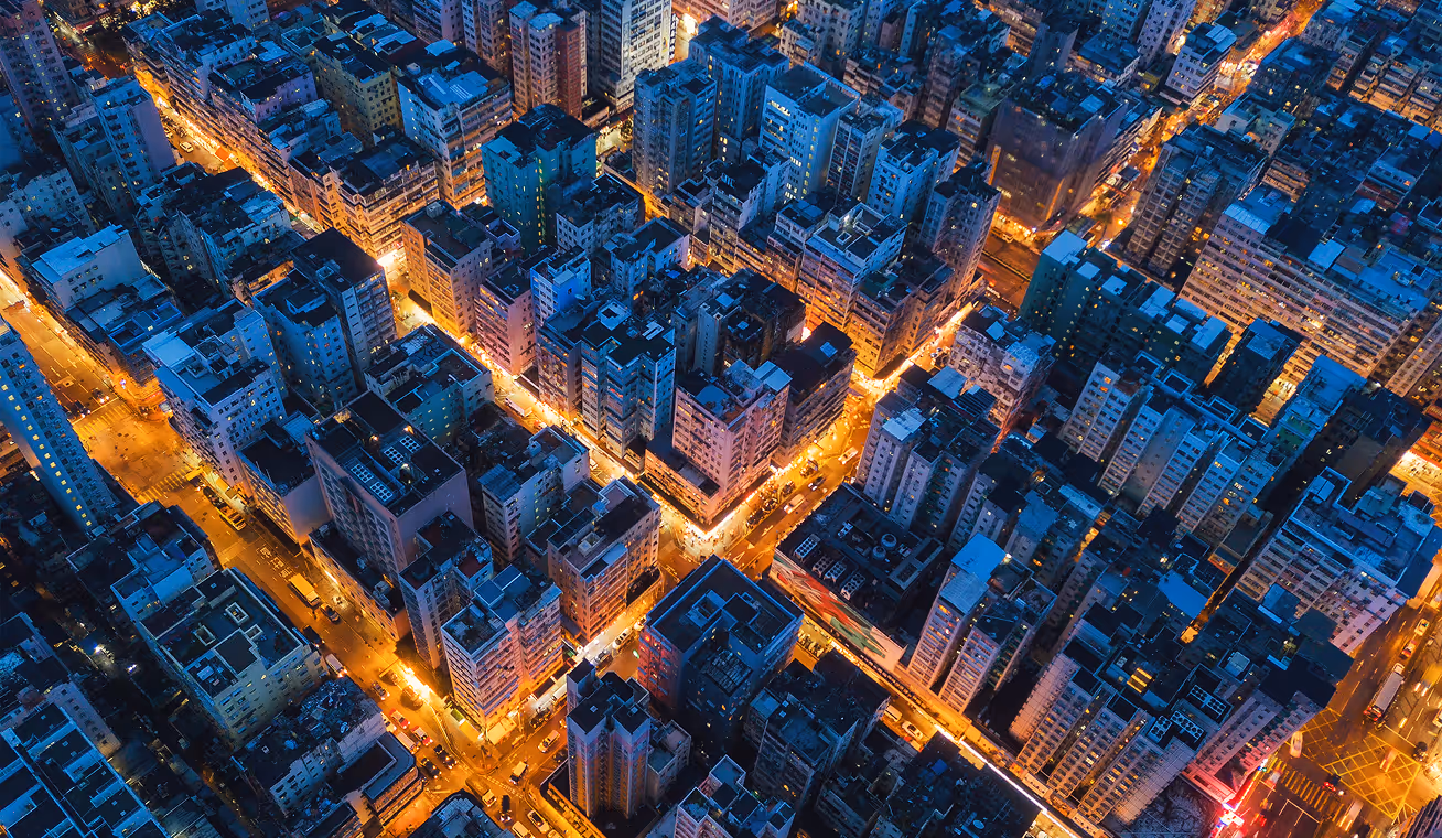 Aerial view of a dense urban city at night with tall buildings and streets lit by orange streetlights.