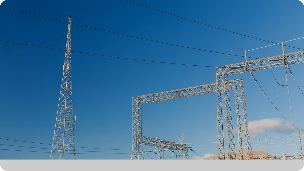 Metal communication tower and electrical transmission structures against a clear blue sky.
