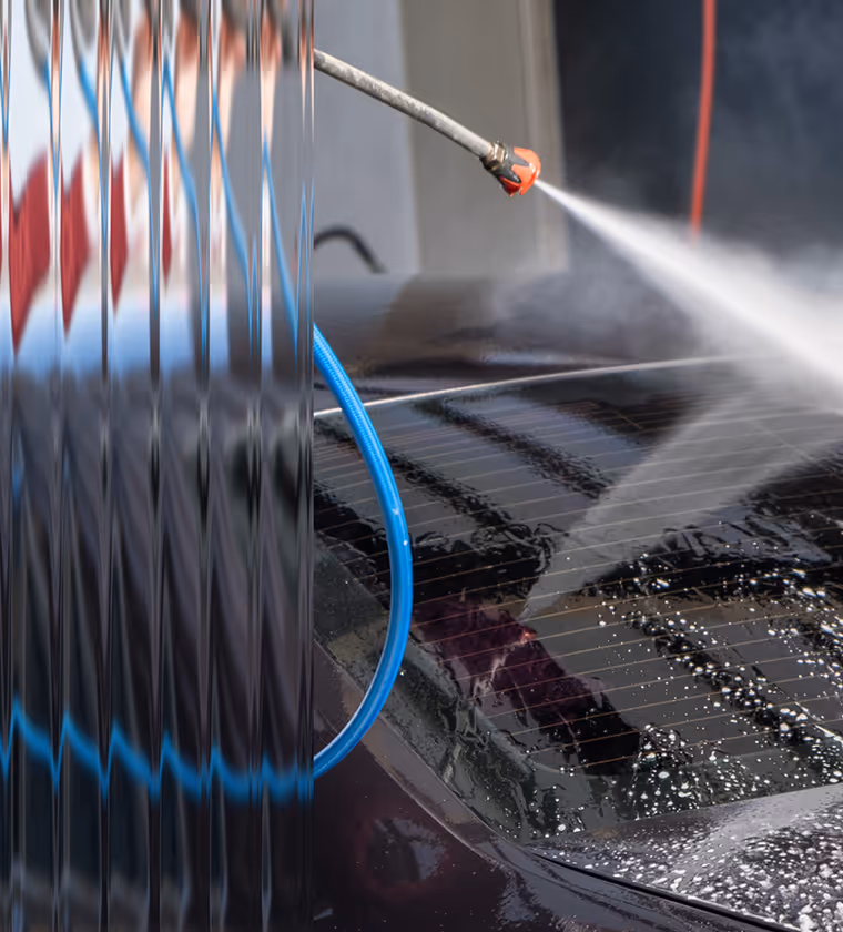 Pressure washer spraying water on the rear window of a black car during cleaning.