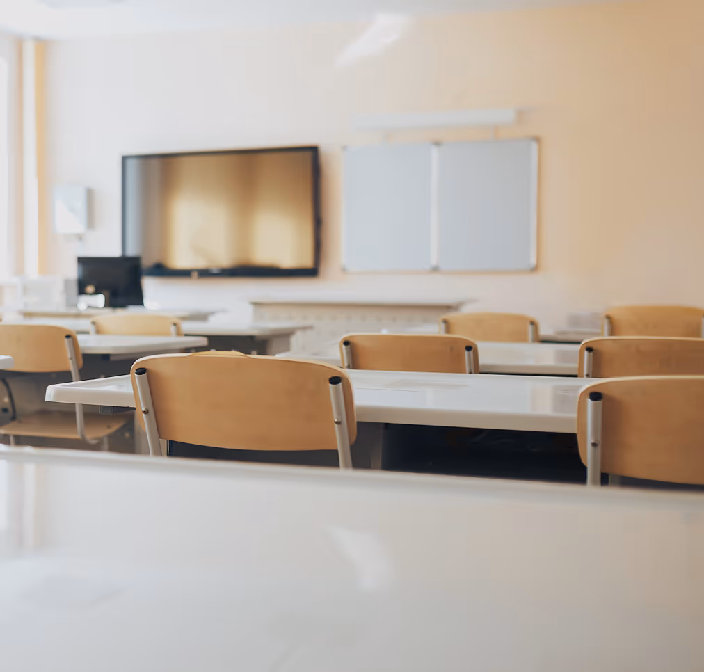 Empty classroom with wooden chairs, white desks, a large screen, and whiteboards on the wall.