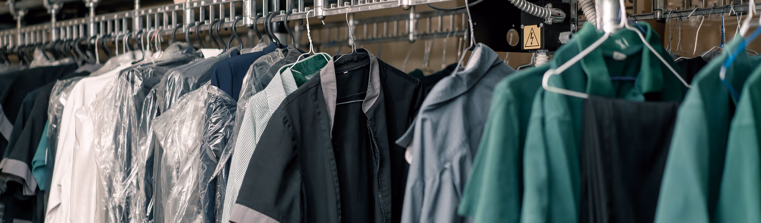 Various garments including shirts and jackets hanging on a dry cleaning conveyor rack, some covered with plastic.