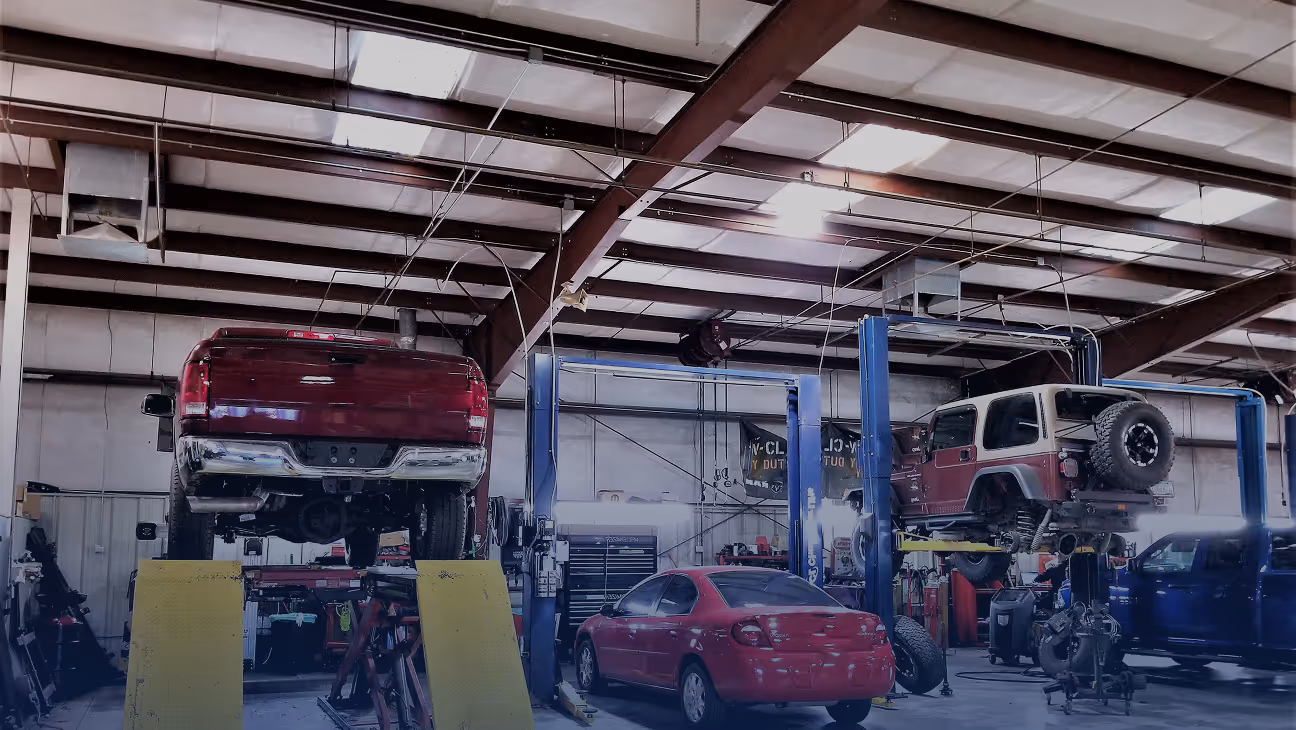 Interior of an auto repair garage with trucks and a red car, some vehicles elevated on lifts for maintenance.