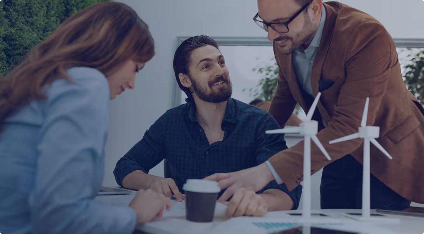 Three colleagues discussing wind turbine models at a table during a meeting.
