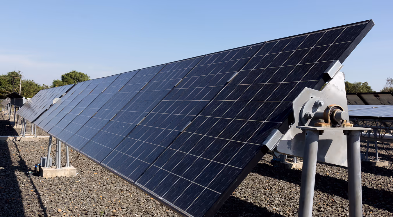 Row of solar panels installed outdoors on a gravel ground under a clear blue sky.