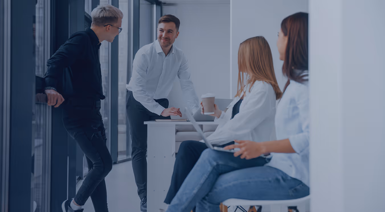 Four young professionals engaged in a casual discussion in a modern office near large windows.