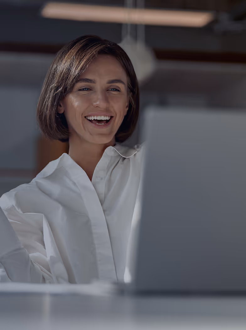 Smiling woman with short brown hair wearing a white shirt looking at a laptop screen.