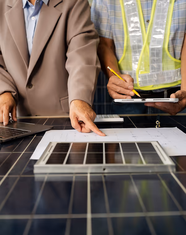 Two people reviewing solar panel plans, one pointing at documents and the other holding a tablet with a pencil.