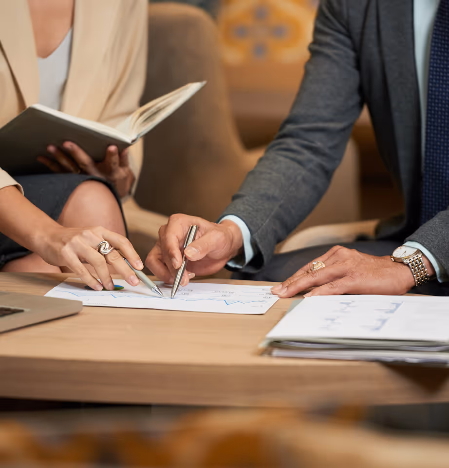 Two business professionals pointing at documents with pens during a meeting.