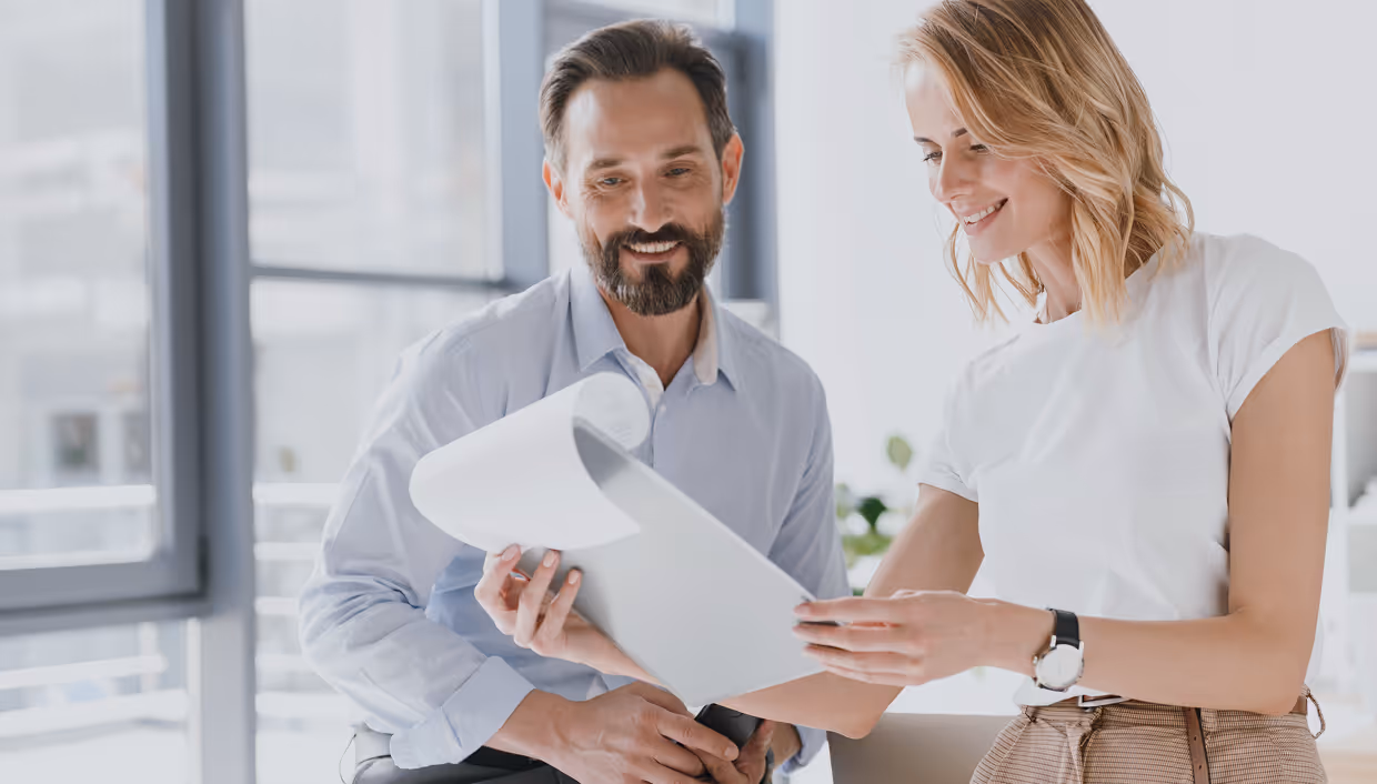 Smiling man and woman reviewing documents together in a bright office.