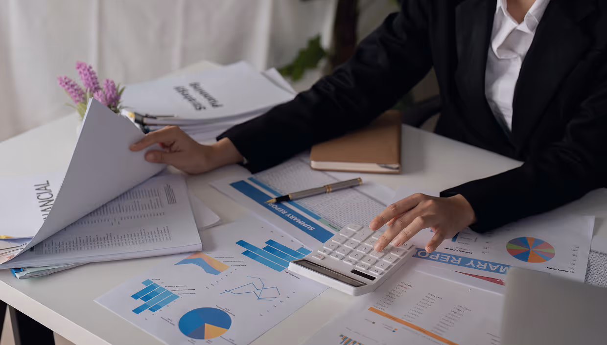 Person in a suit working at a desk with financial documents, charts, and a calculator.