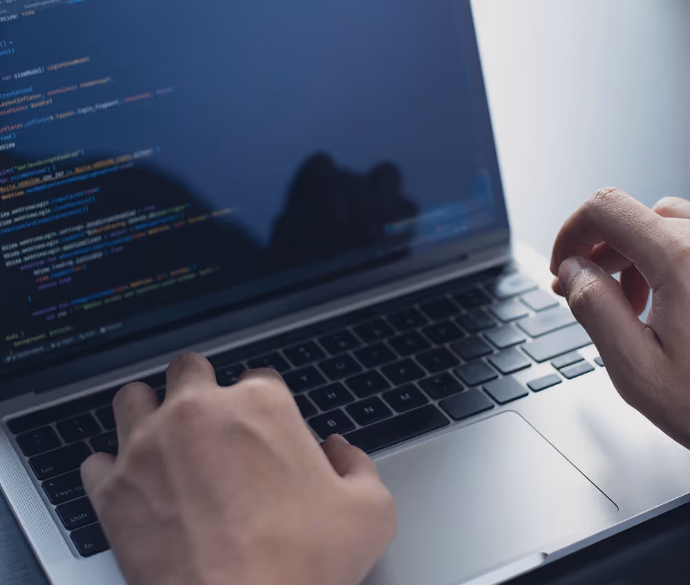 Person typing code on a laptop keyboard with programming code visible on the screen.