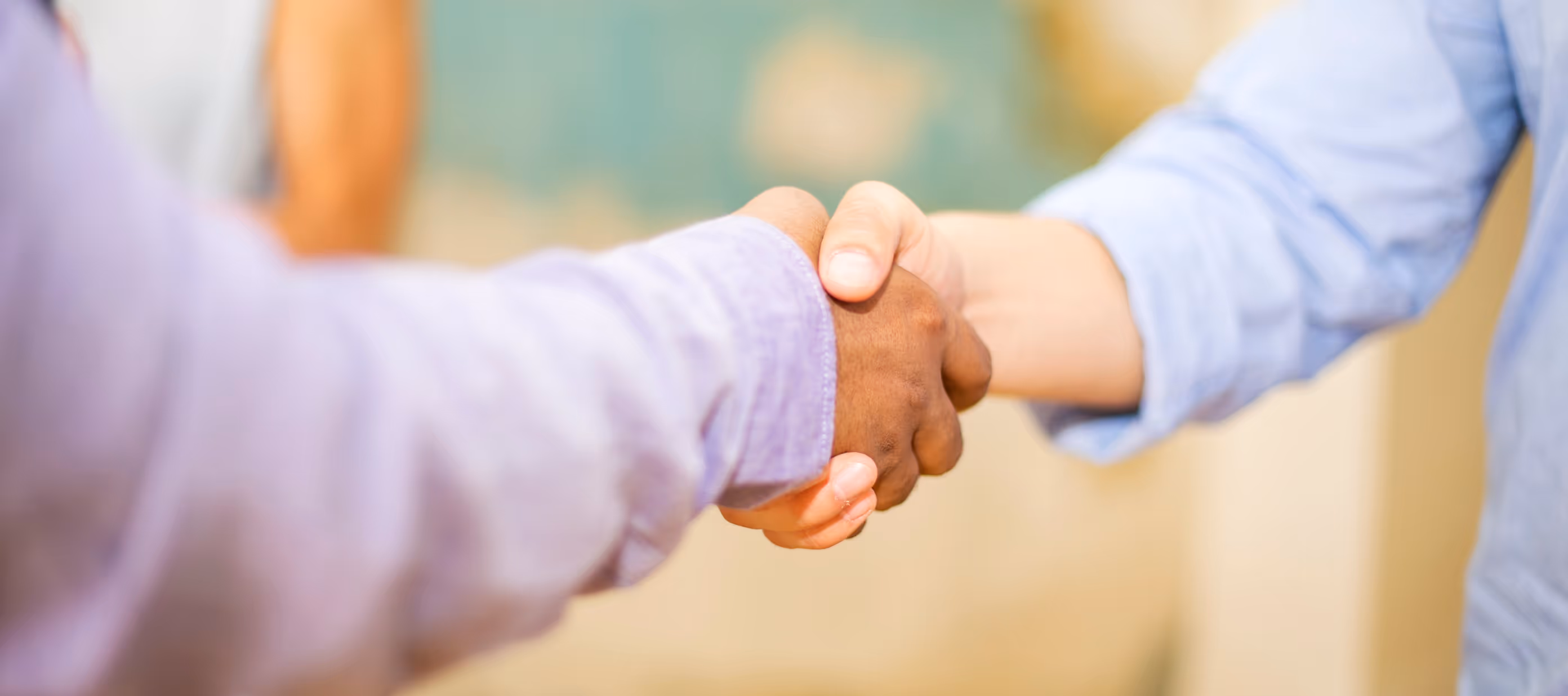 Close-up of two people shaking hands, one wearing a purple shirt and the other a light blue shirt.