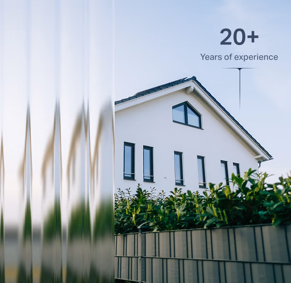 Модерна бяла къща с черен покрив и ограда с храсти, с надпис 20+ години опит.