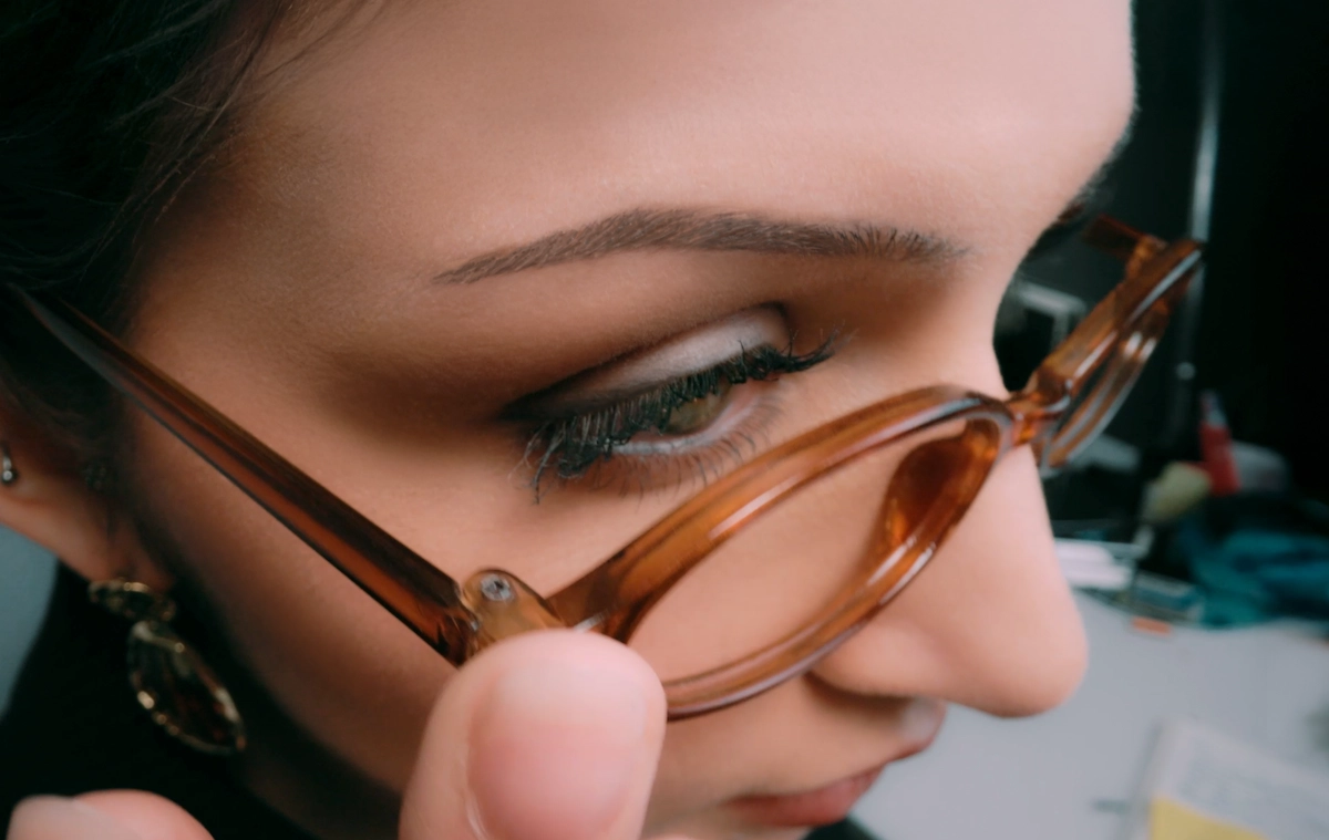 Close-up of a woman adjusting her brown-framed glasses with her hand.