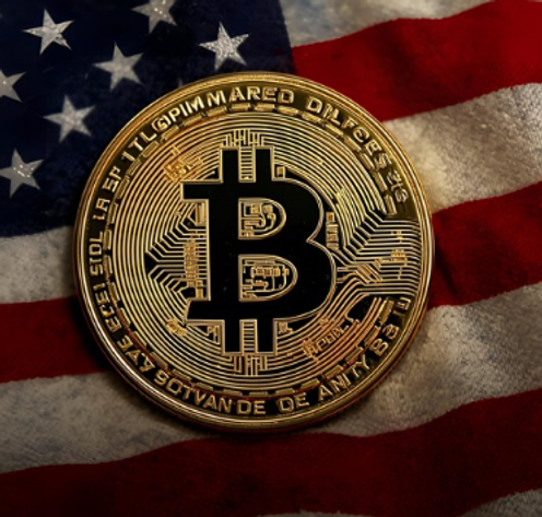 Bitcoin coin on a wrinkled American flag. The gold coin features a large 'B' symbol. The flag's stars and stripes are visible.