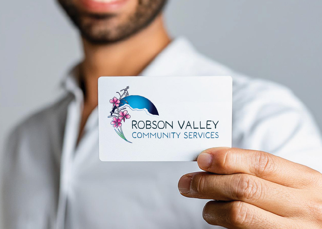 Person holding a card with Robson Valley Community Services logo featuring mountains and pink flowers.