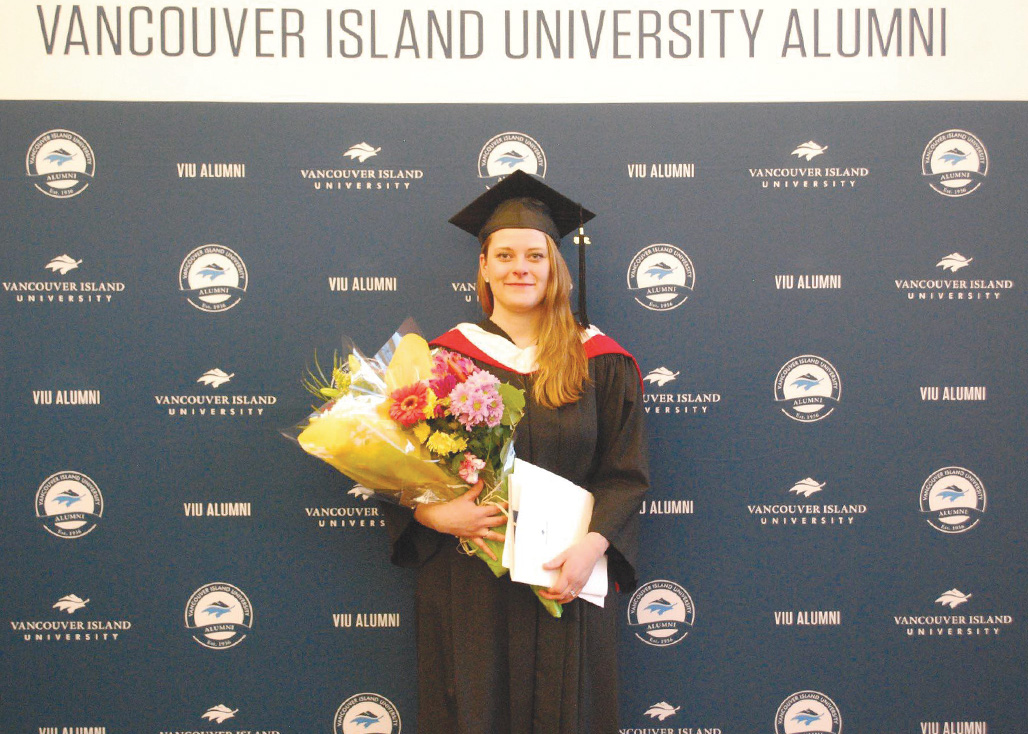 Vancouver Island University graduate in cap and gown holding bouquet and diploma folder.