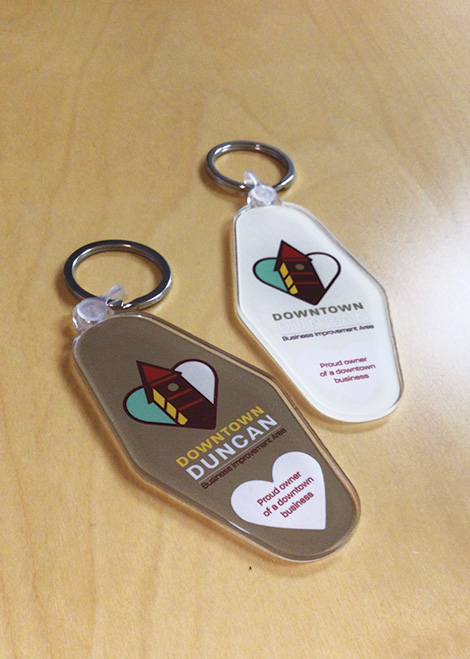 Two Downtown Duncan keychains with logo and text on a wooden surface.