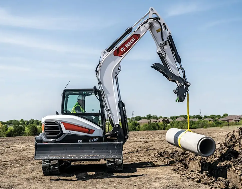 Excavator laying large drainage pipes on active construction site