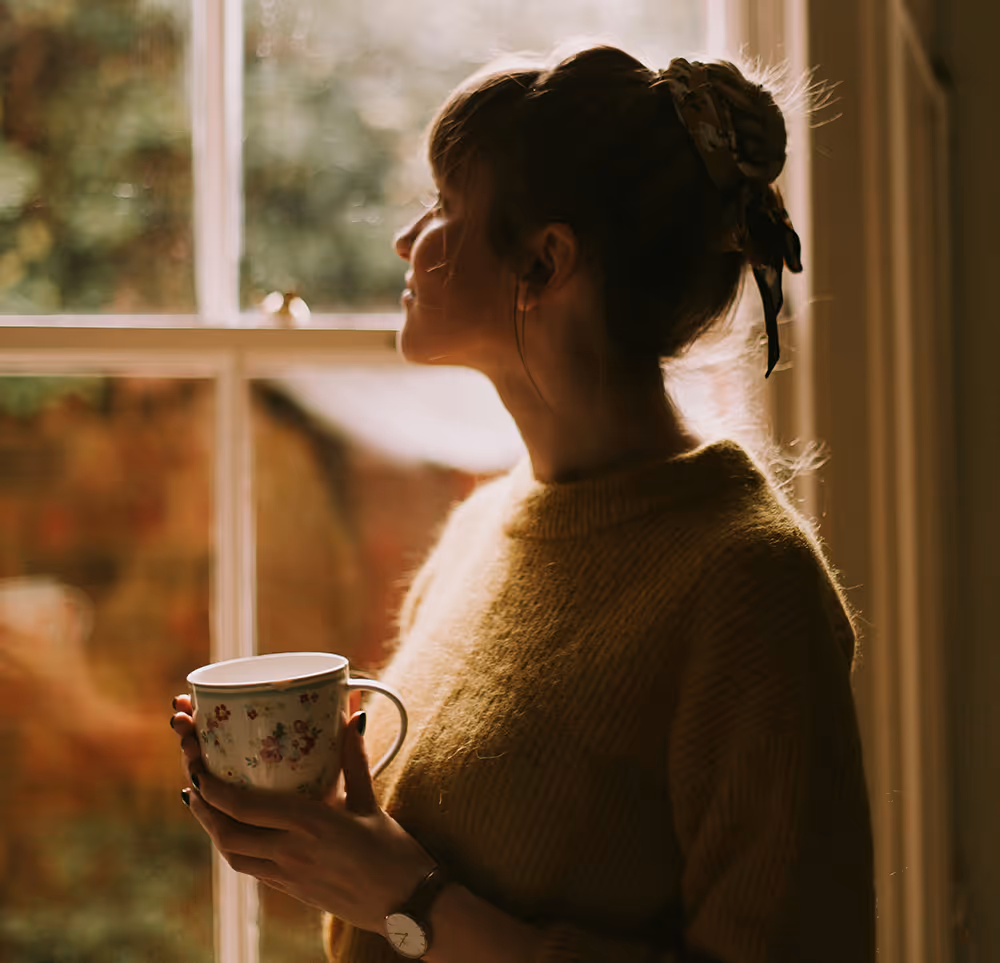 Woman relaxing at home holding a cup of tea by the window