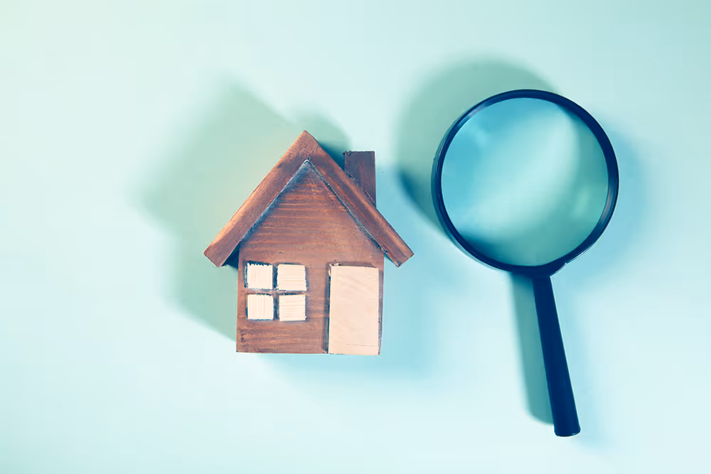 Magnifying glass beside a model house representing searching UK mortgage lenders
