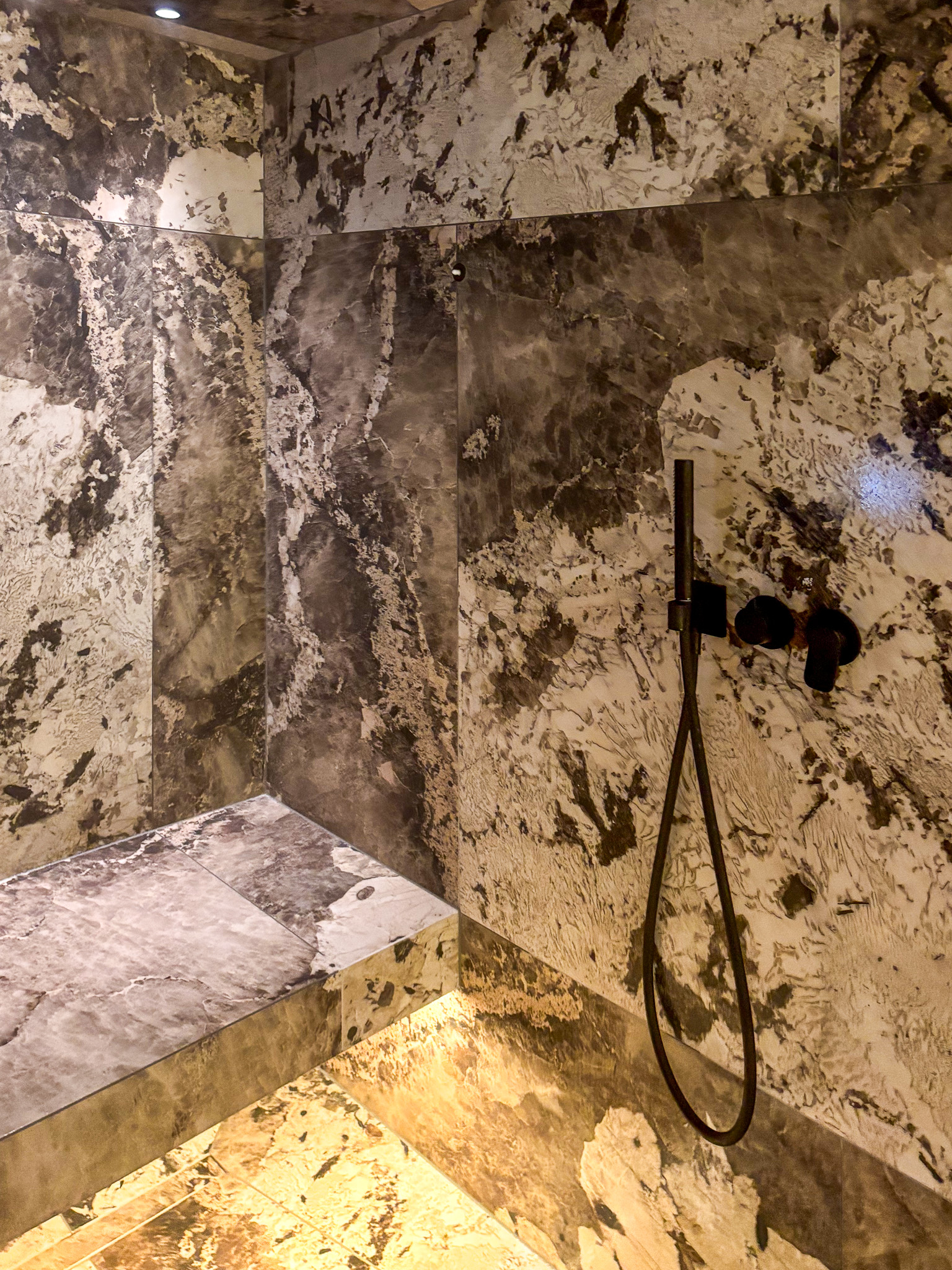 Dampfbad mit marmorierten Oberflächen und schwarzen Armaturen – exklusives Wellnessdesign für Zuhause
