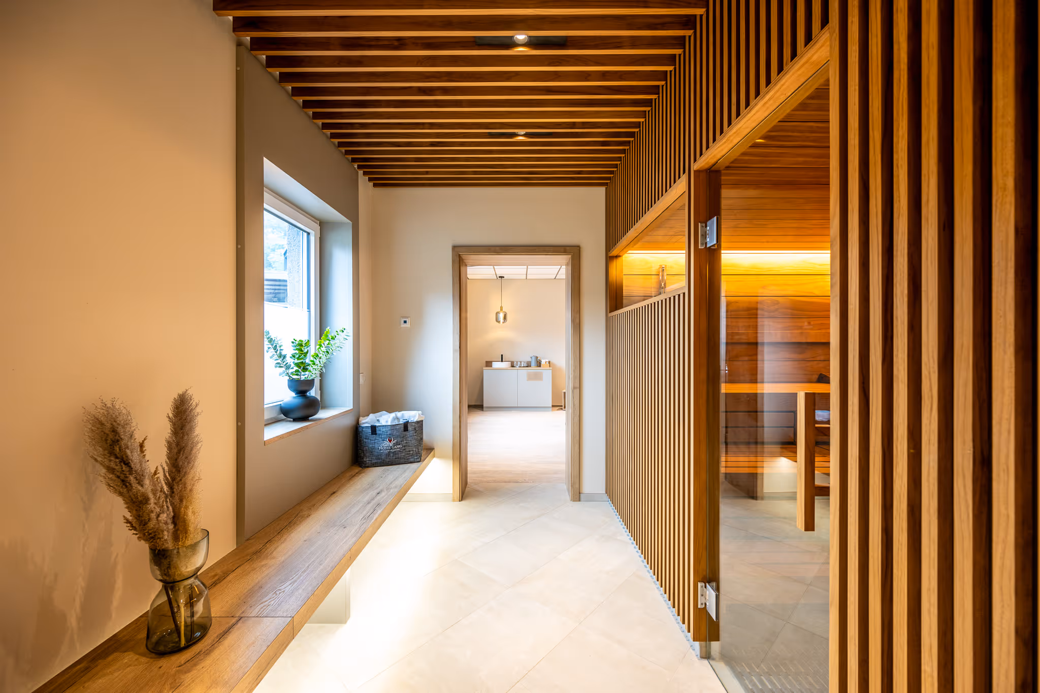 Moderner Saunavorraum mit Holzdetails, Bank, Vase mit Pflanzen und Eingang zur finnischen Sauna.
