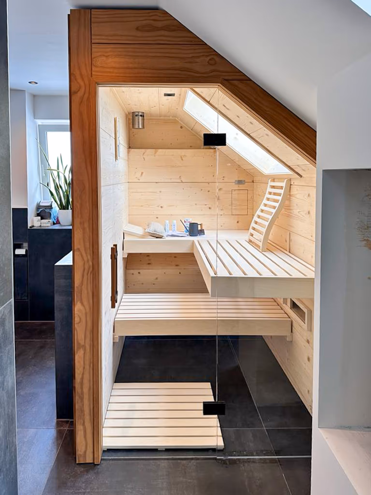 Moderne helle Sauna aus hellem Holz mit schrägem Dachfenster und bequemen Sitzbänken.