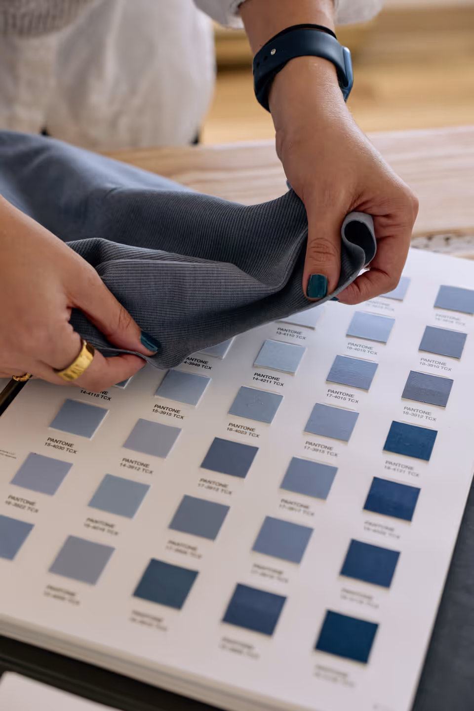 Person holding a grey fabric swatch over a Pantone colour chart with various blue shades.