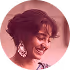 Smiling woman with short curly hair wearing large earrings and a purple top against a blurred background.