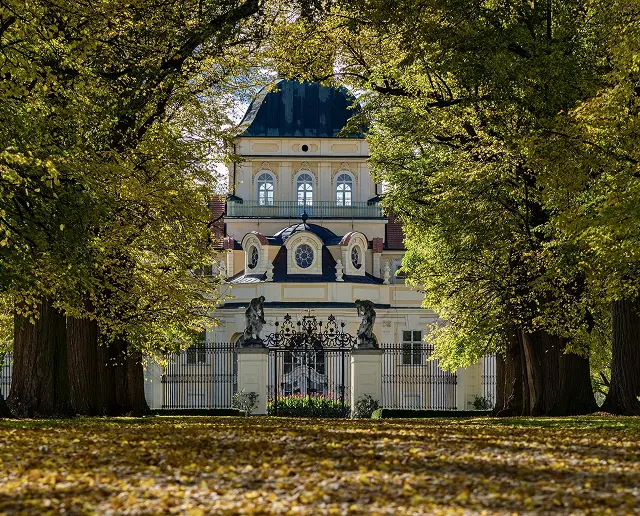 Château majestueux, portail visible entre des arbres, symbolisant la découverte du patrimoine culturel.