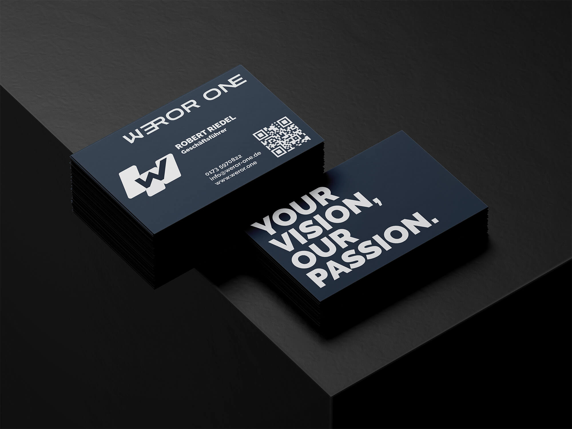 Zwei Stapel von Weror One Visitenkarten, eine mit Kontaktdaten von Robert Riedel, Geschäftsführer, und eine mit dem Slogan 'Your Vision, Our Passion'.