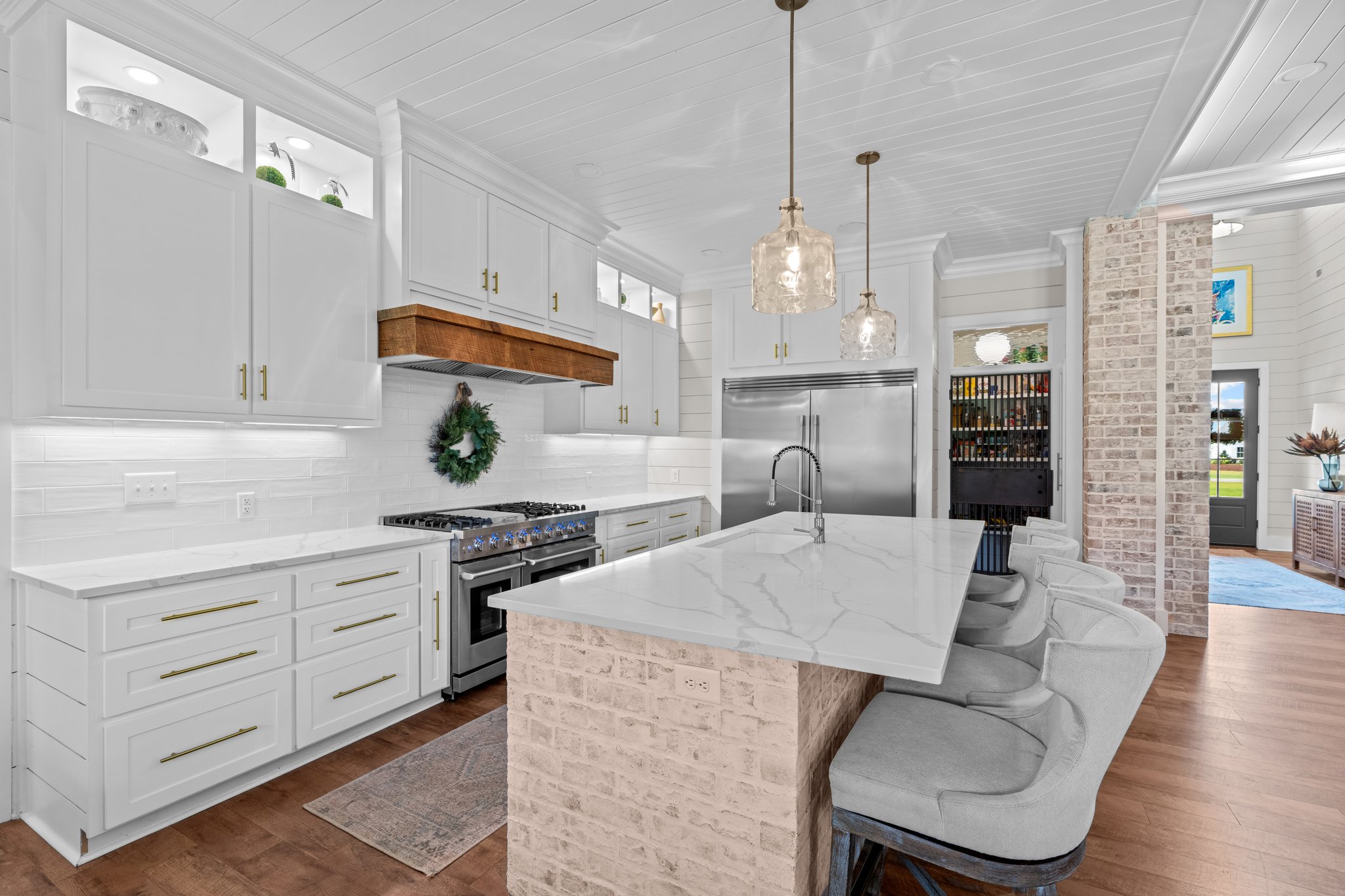 Modern white kitchen with marble island, brick accents, and hanging pendant lights