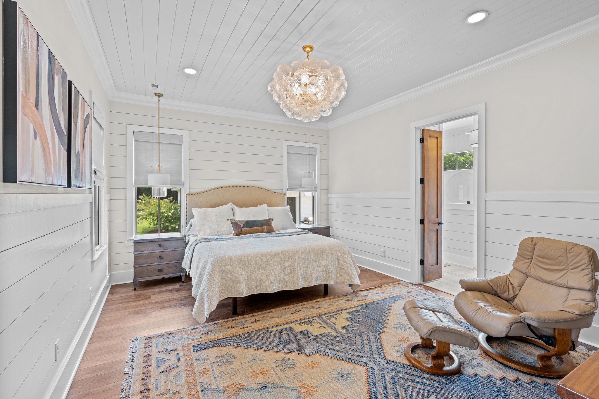 Bright bedroom with shiplap walls, elegant chandelier, and cozy reading chair