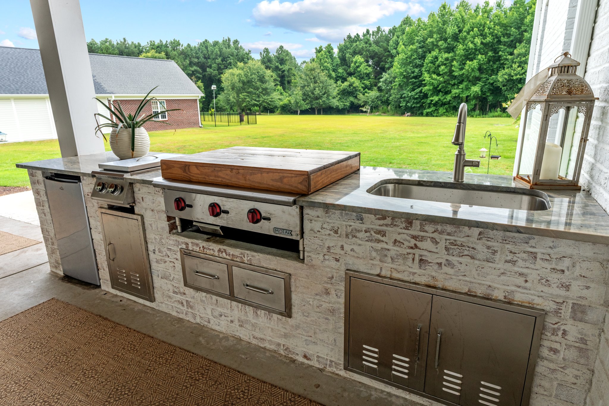 Outdoor kitchen with grill, sink, and countertop on patio with green backyard
